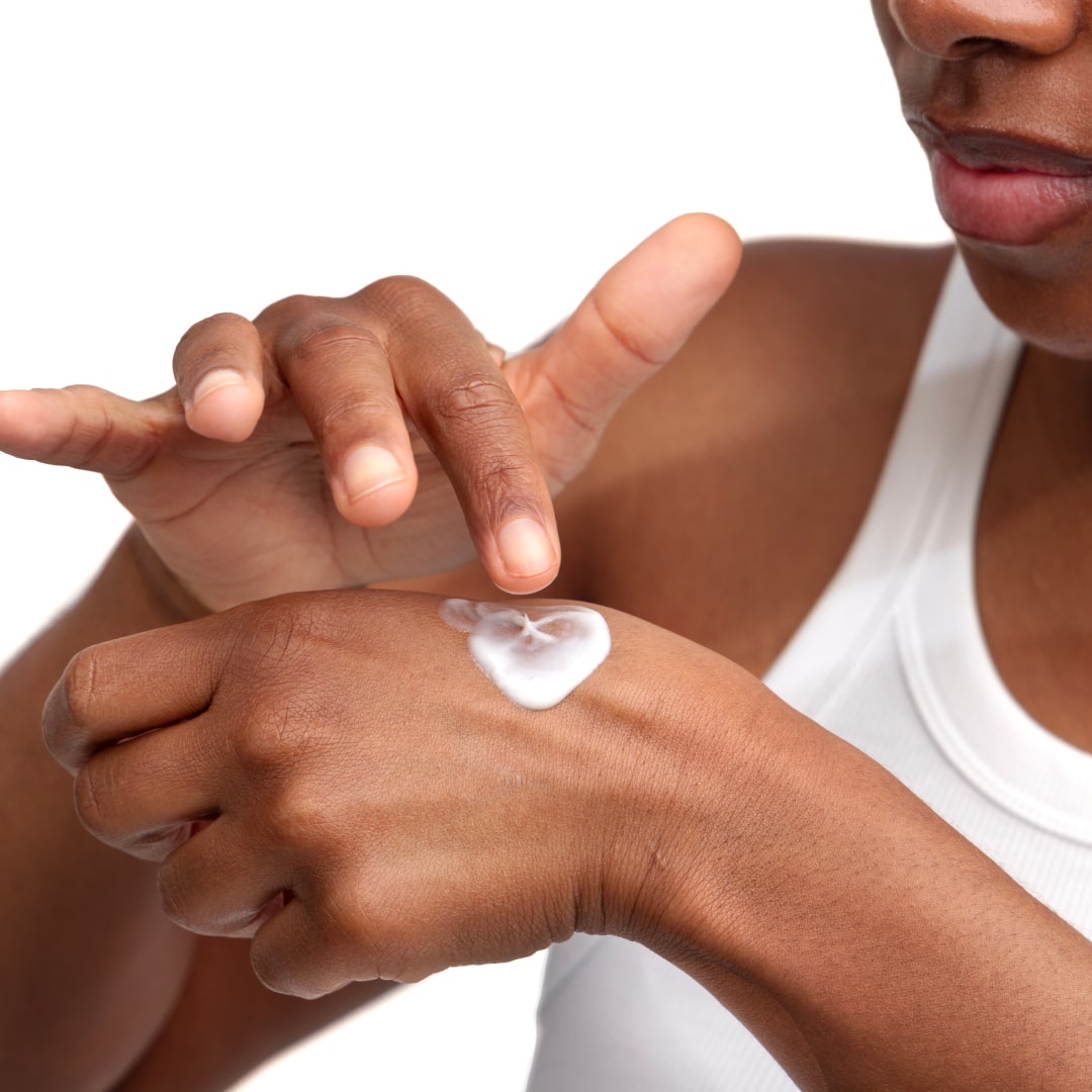 Woman has a bit of the Biome Barrier on the back of her hand and is dabbing her finger into it so as to apply some of it on the face. The Biome barrier is a microbiome and skin barrier supporting cream formulated by Dr. Liv Kraemer; the cream also  moisturizes the skin.