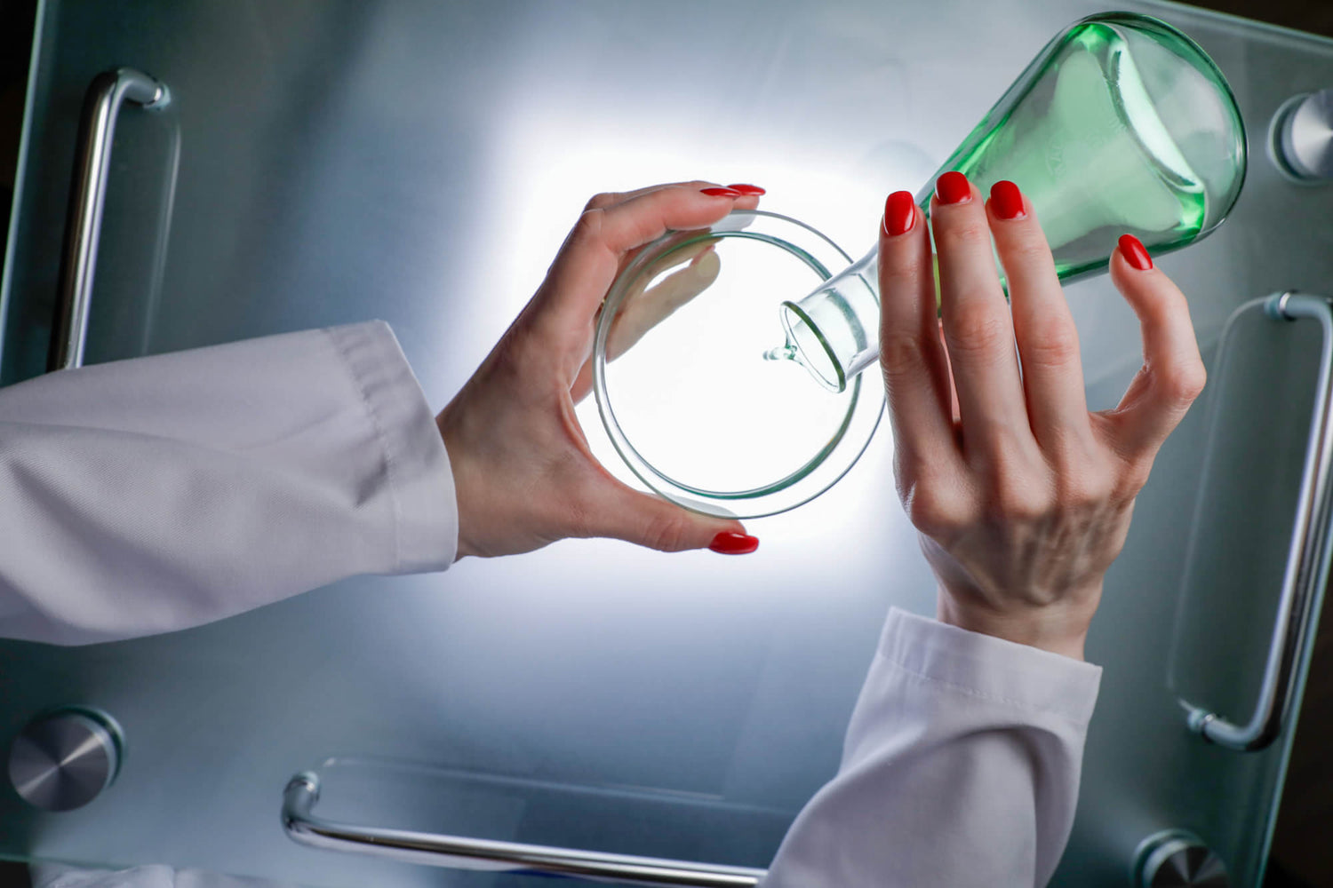 Close up of the hands of board certified dermatologist and longevity skincare specialist Dr. Liv Kraemer filling liquid from a conical flask into a petri dish.