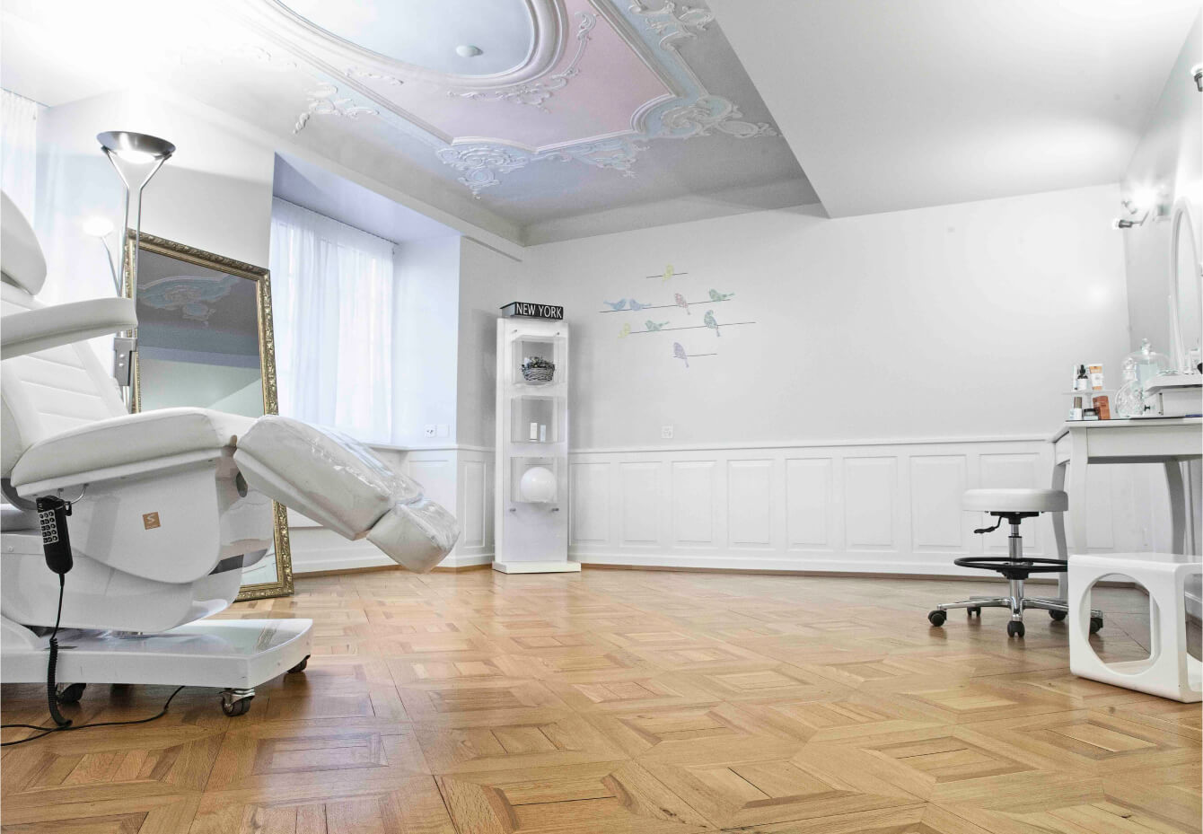 The treatment room with a white doctors chair and an inviting ambiance from the board certified dermatologist and longevity skincare expert dr. Liv Kraemer Longevity Clinic is shown with wooden floors and an ornamented ceiling.