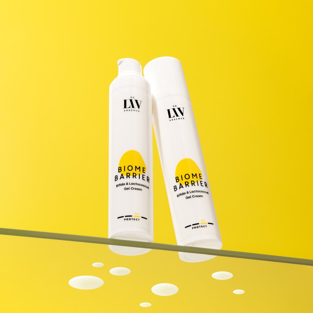 Two Packages of the probiotic, moisturizing Biome Barrier cream for the face developed by board certified dermatologist and skin longevity expert Dr. Liv Kraemer are standing on glass in front of a yellow background.