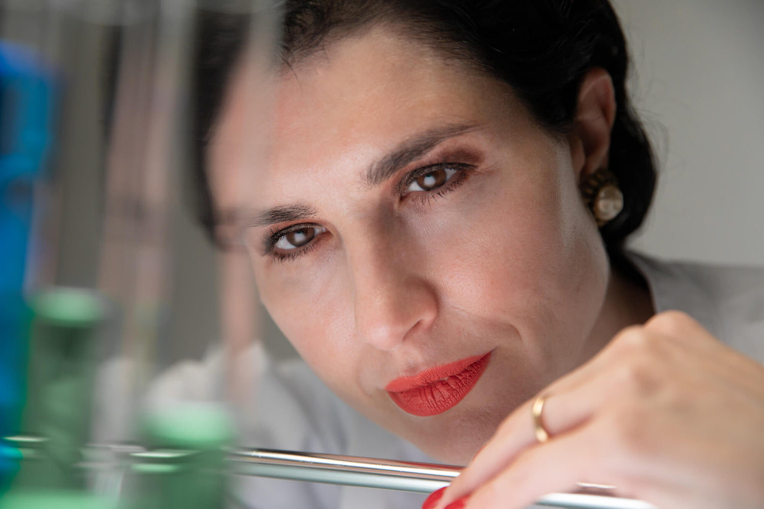 Board certified dermatologist and longevity skincare specialist Dr. Liv Kraemer in a close up frame is wearing a white lab coat while examining test tubes.