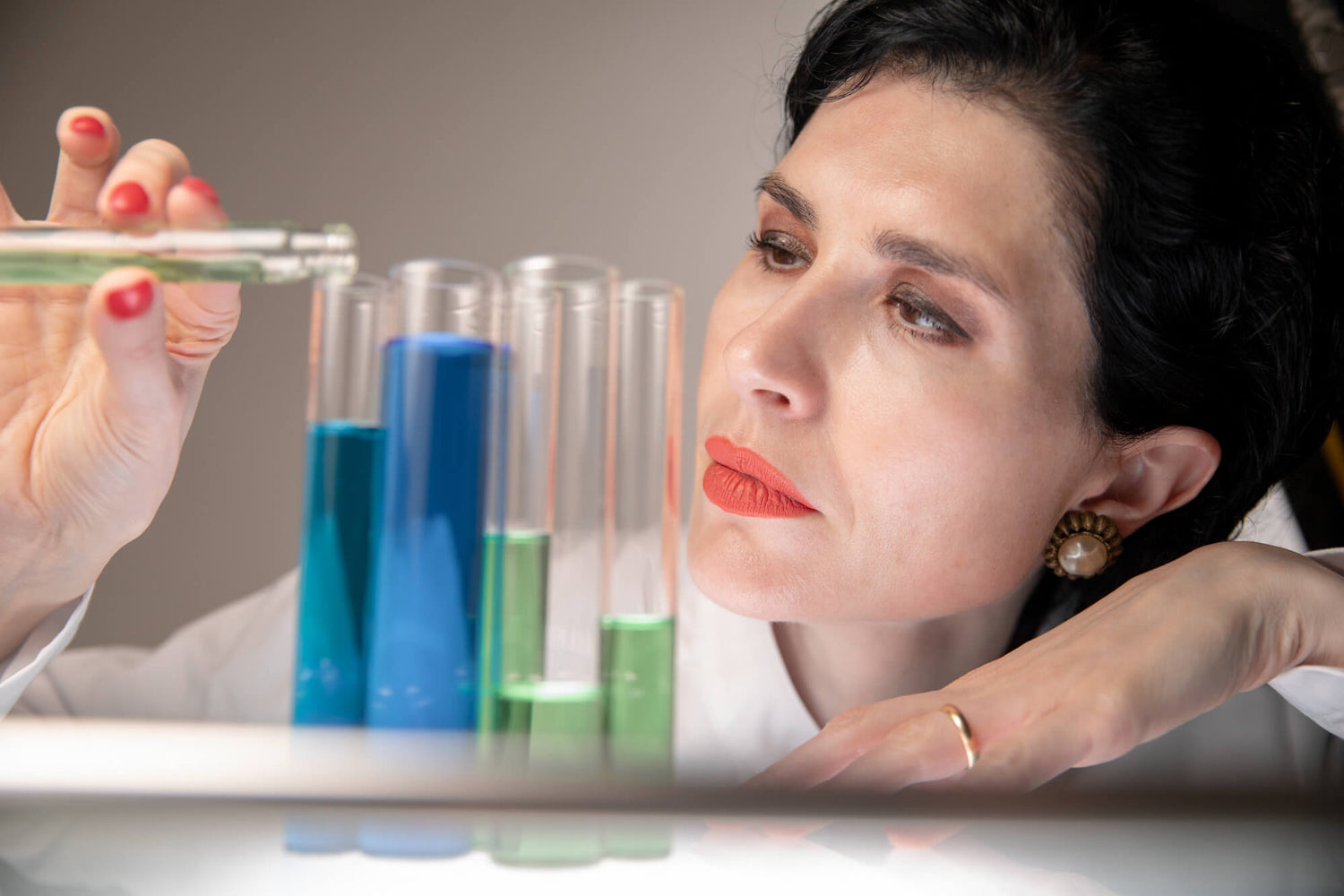 Board certified dermatologist and longevity skincare specialist Dr. Liv Kraemer in a close up frame is wearing a white lab coat while filling liquid into test tubes.