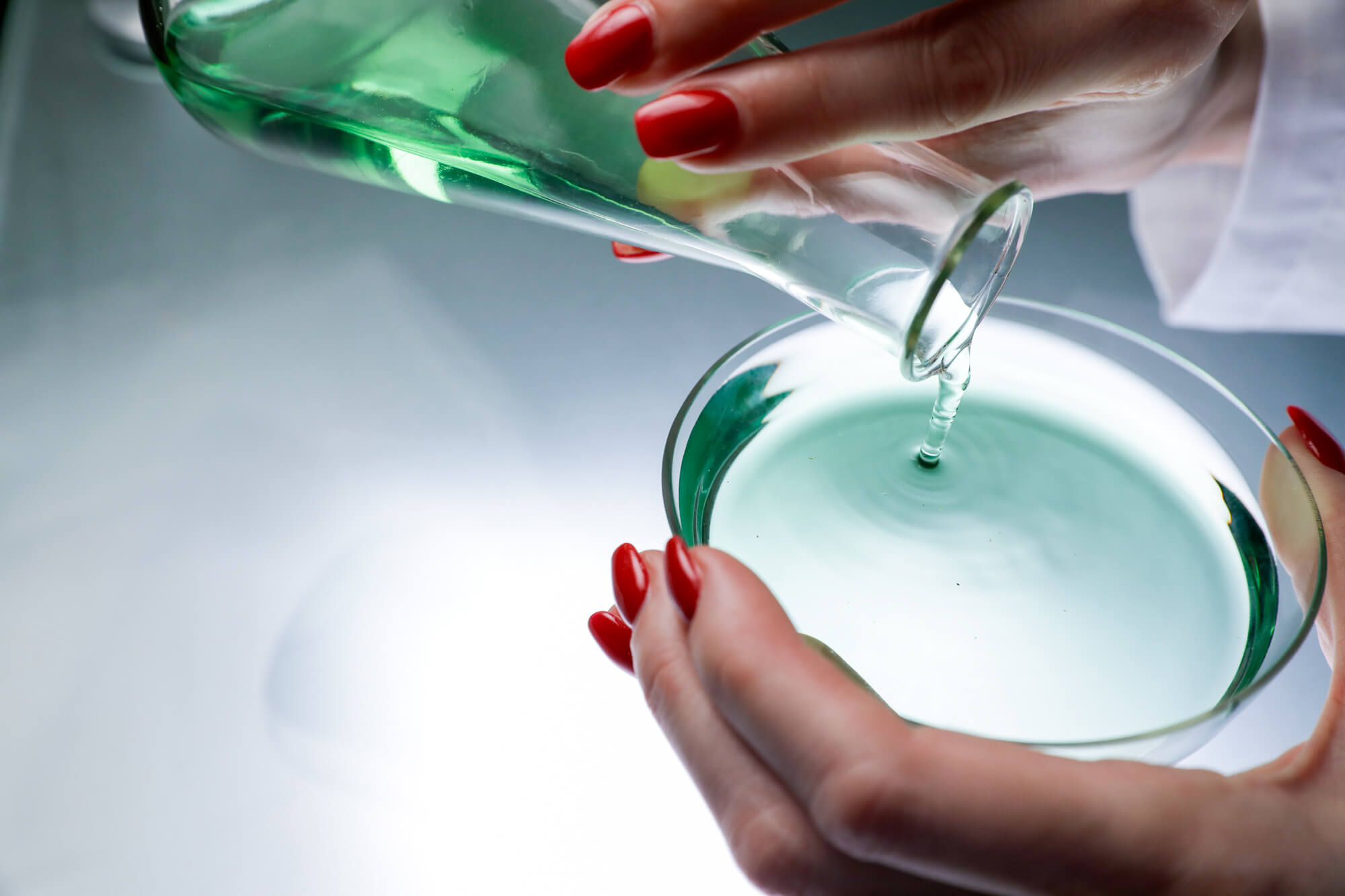 Close up of the hands of board certified dermatologist and longevity skincare specialist Dr. Liv Kraemer filling liquid from a conical flask into a petri dish.