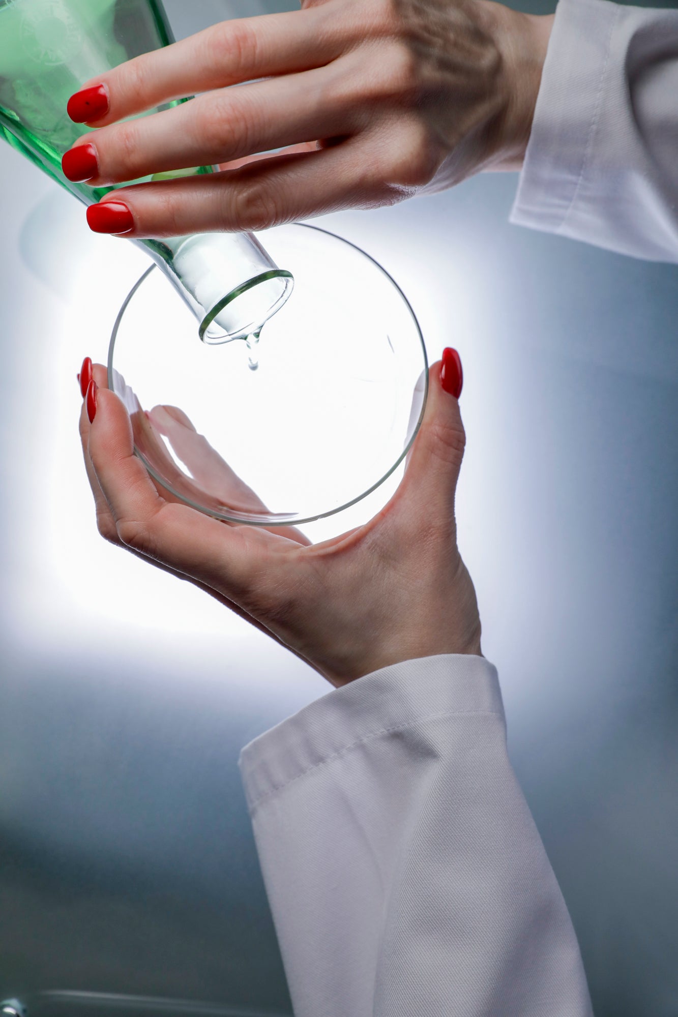 Close up of the hands of board certified dermatologist and longevity skincare specialist Dr. Liv Kraemer filling liquid from a conical flask into a petri dish.